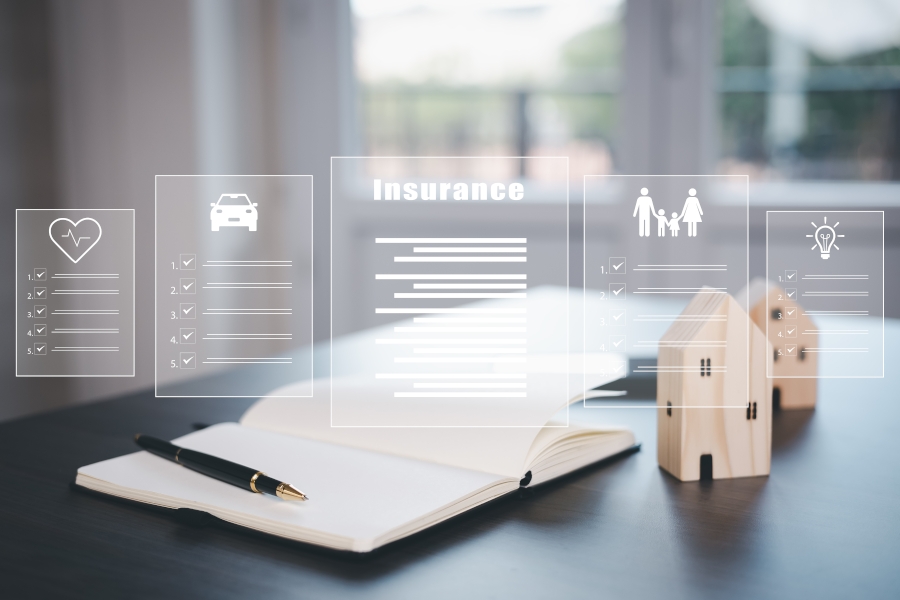 Ein offenes Notizbuch mit einem Stift und kleinen Holzhaus-Modellen. Auf dem Tisch sind digitale Versicherungslisten sichtbar, die verschiedene Kategorien wie Gesundheit, Auto und Familie darstellen.